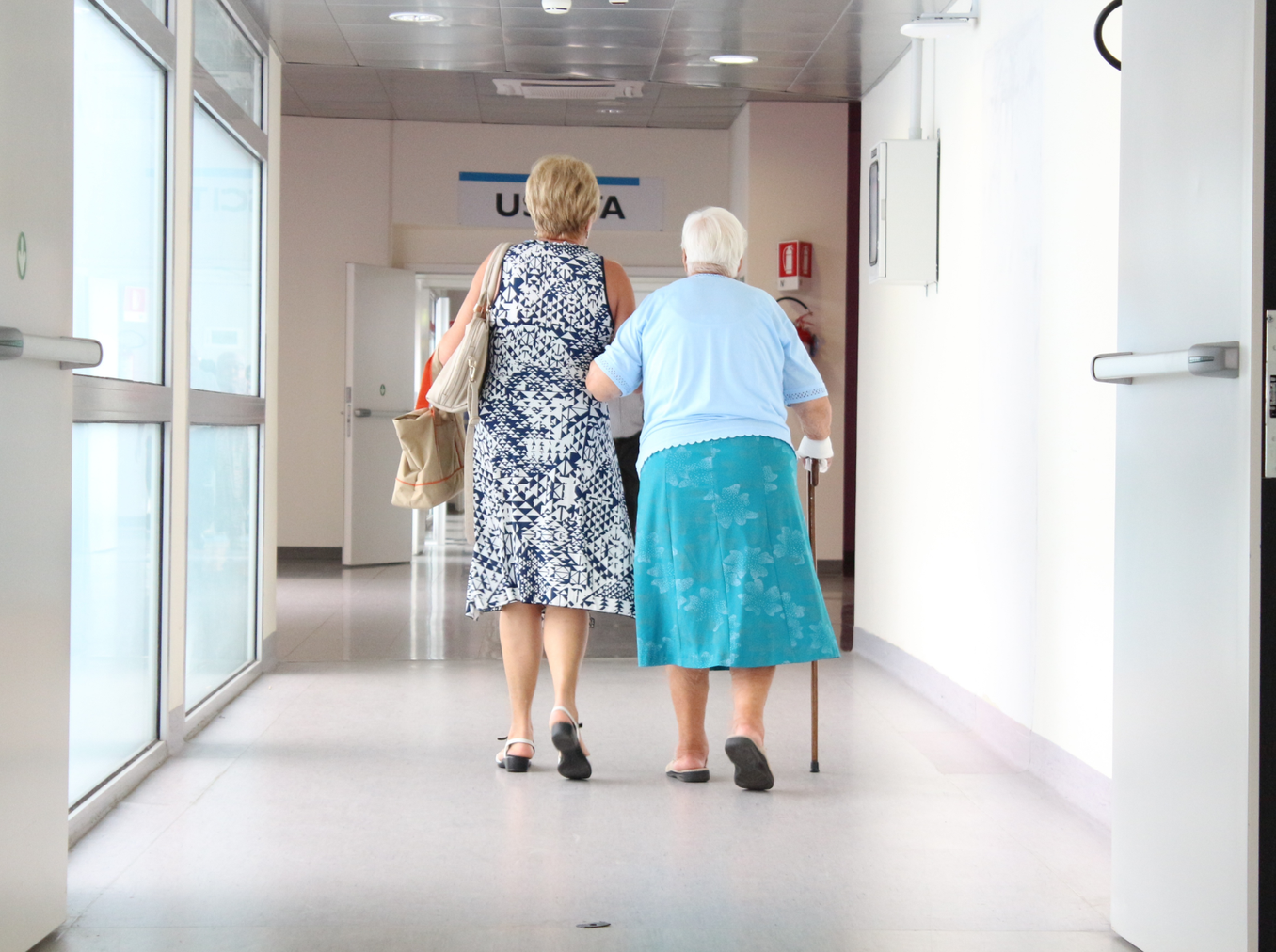 two women walking down a hospital corridor arm in arm