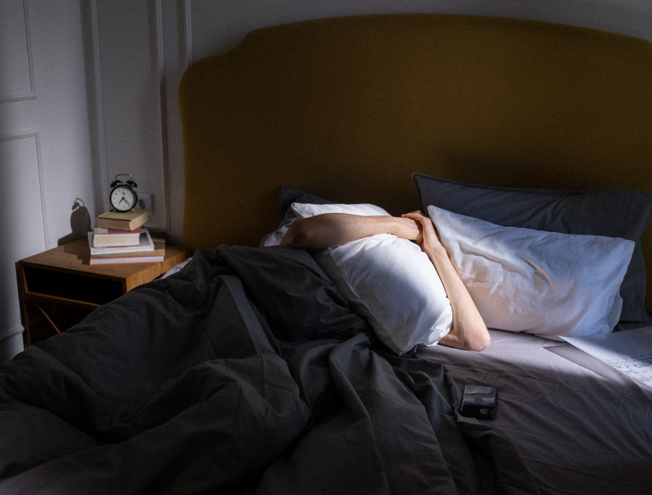 Man burying head under bed covers to hide from sun