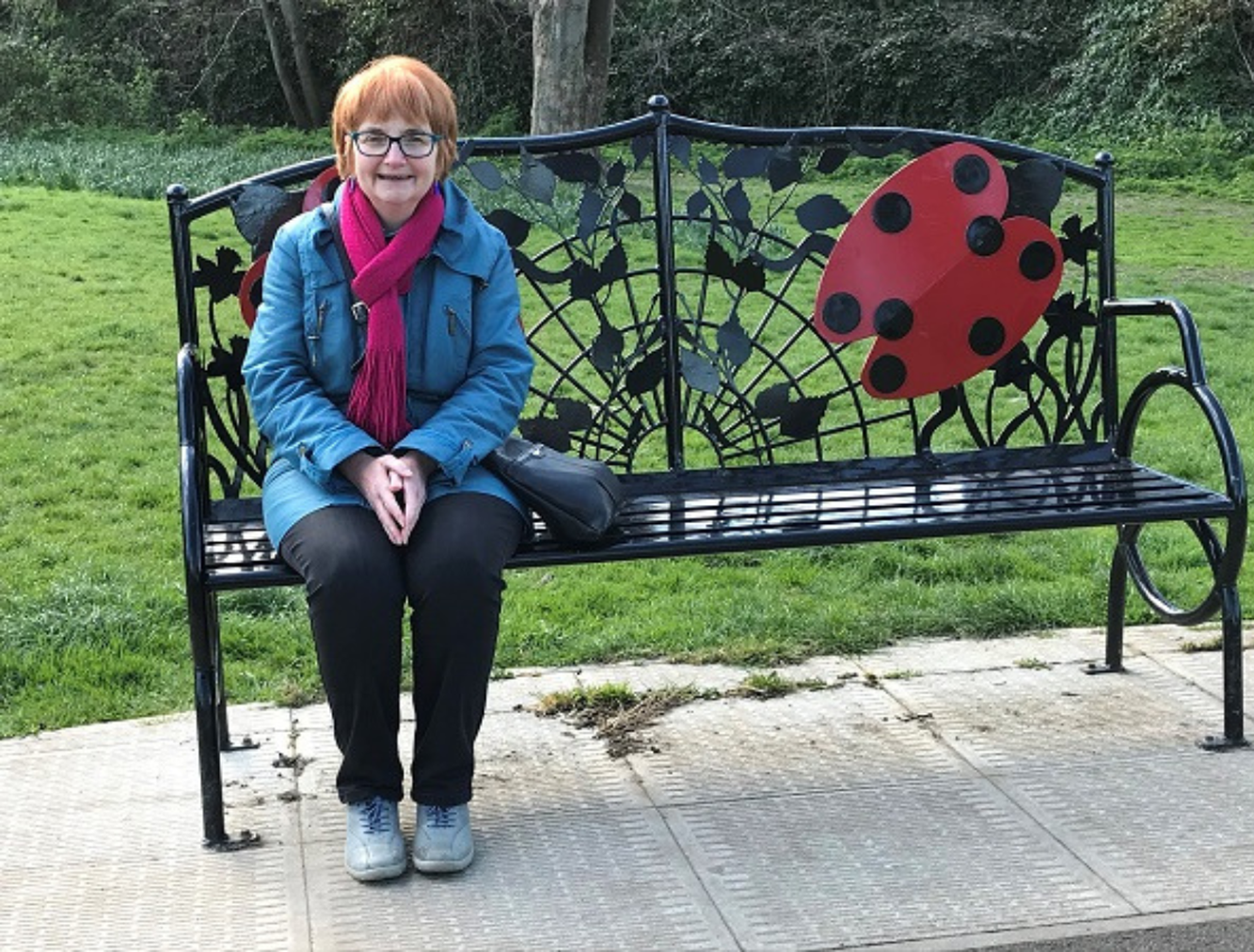 Sheila sat on an outdoor bench smiling at the camera