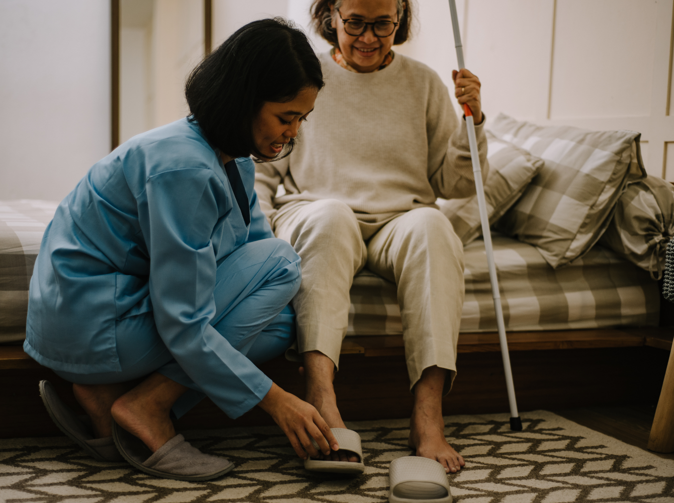 woman helping elderly women put her slippers on, both smiling