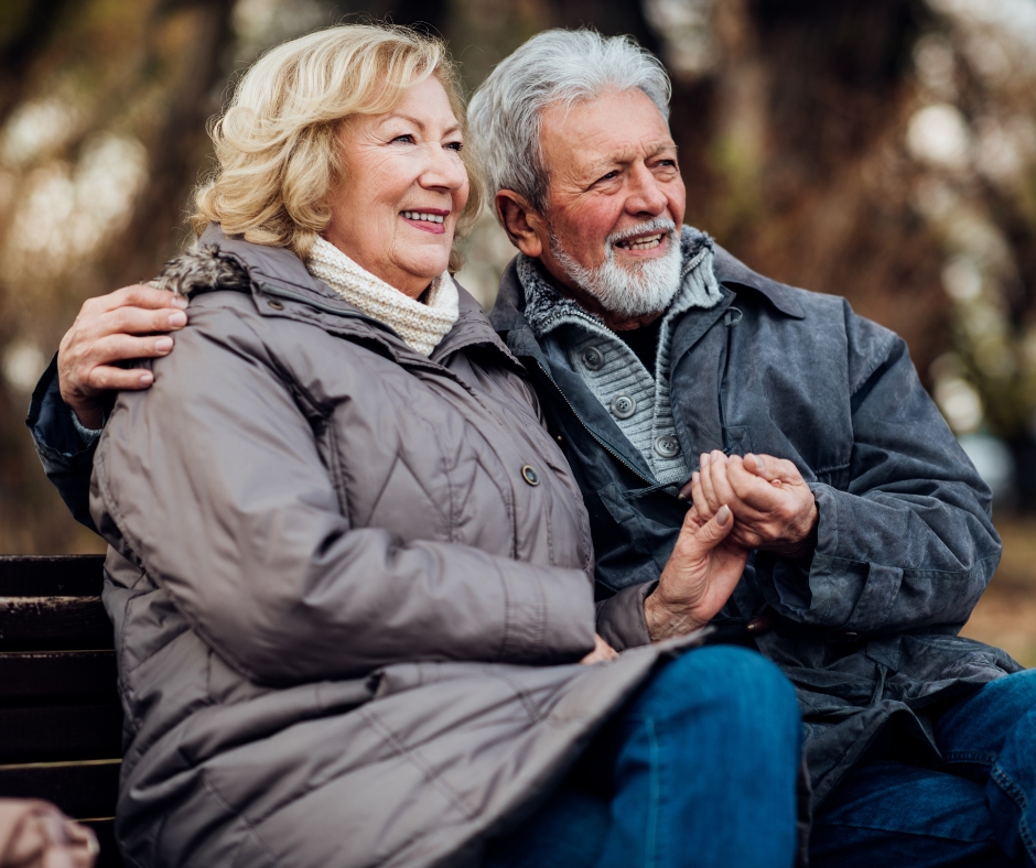 Elderly couple sat holding hands on a park bench