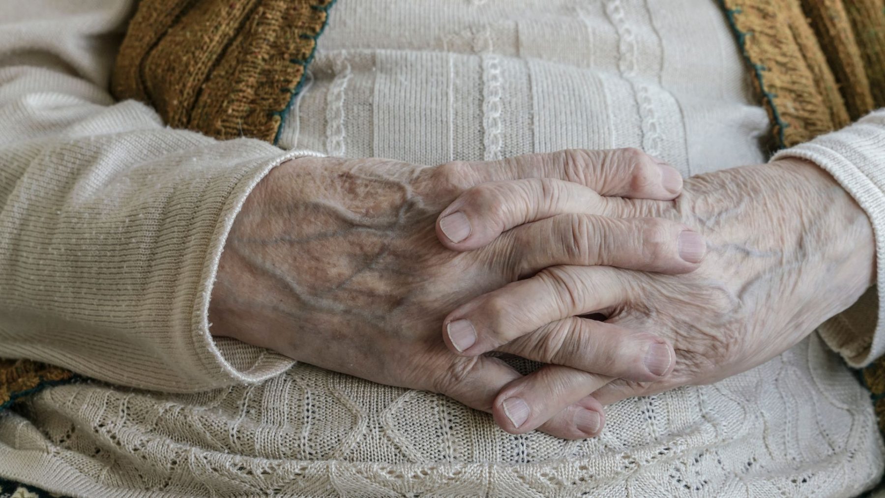 Elderly person reclined with their interlocked fingers resting on their stomach