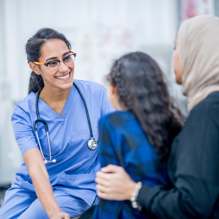 Healthcare professional smiling while speaking with two people.