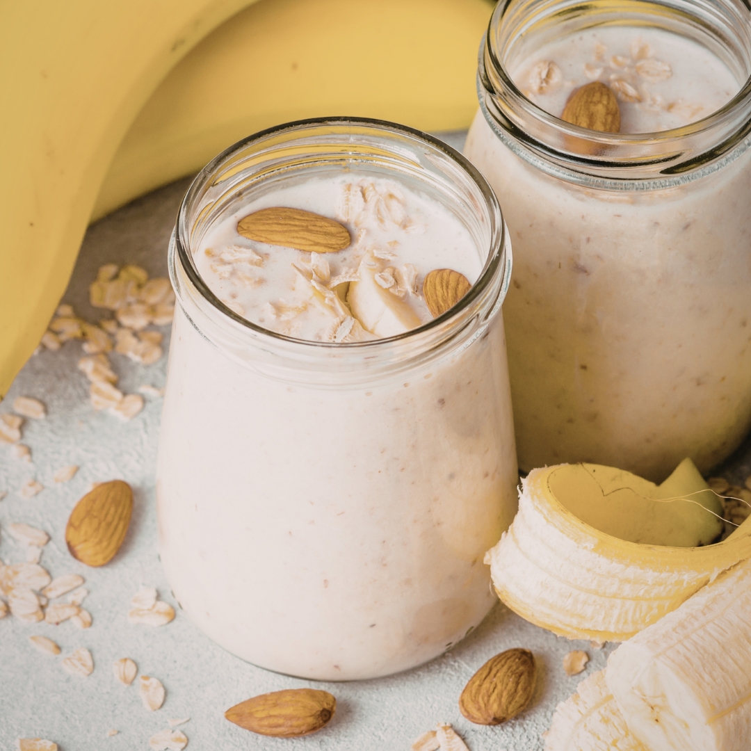 Almond smoothie in glass surrounded by bananas