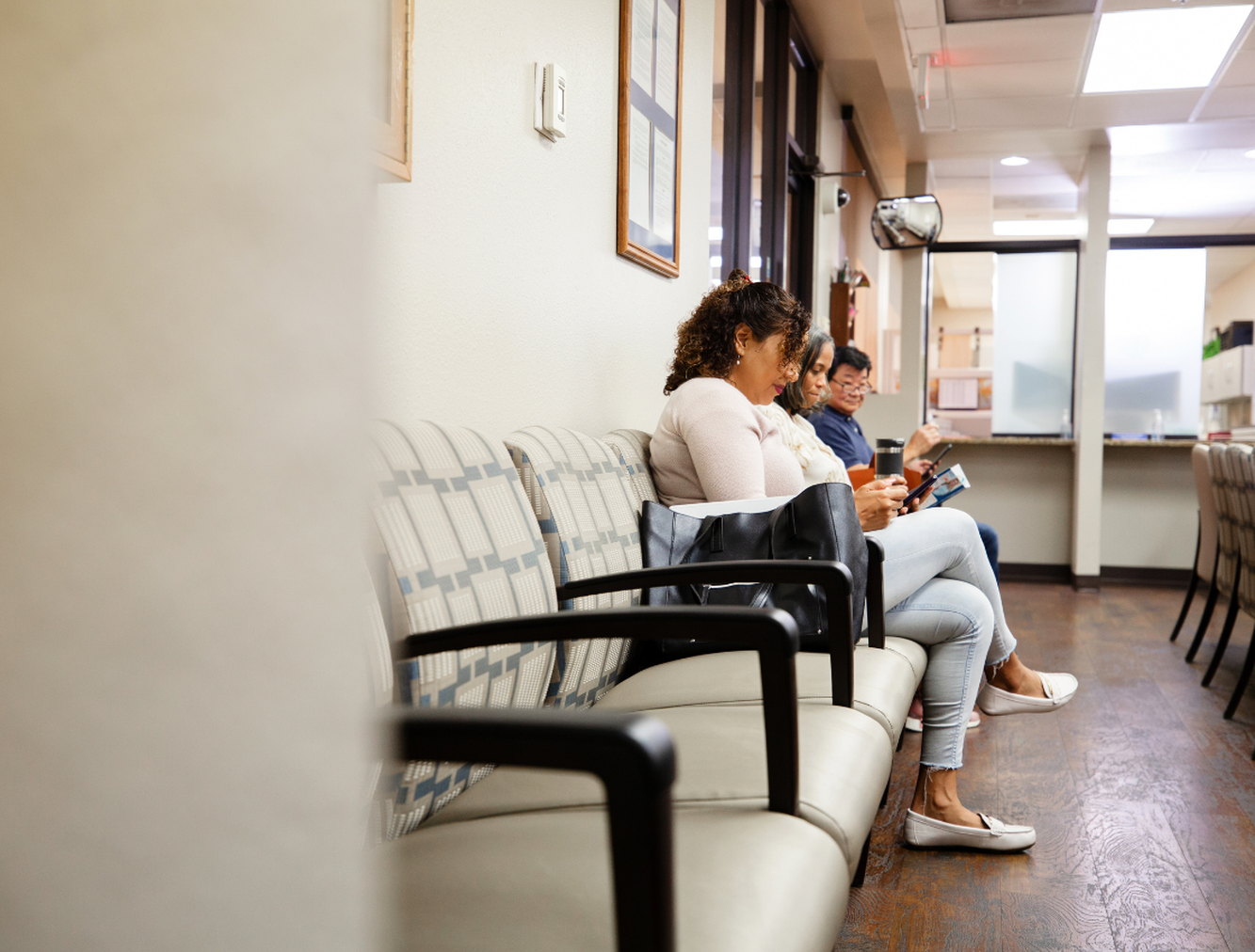 Three people sat on chairs in hospital waiting room