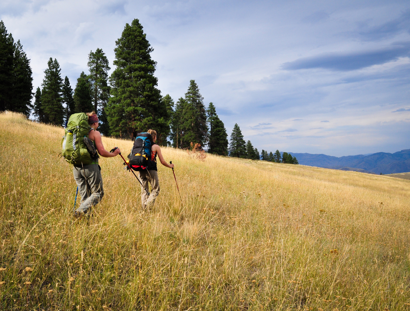 Two women with backpacks trekking through countryside