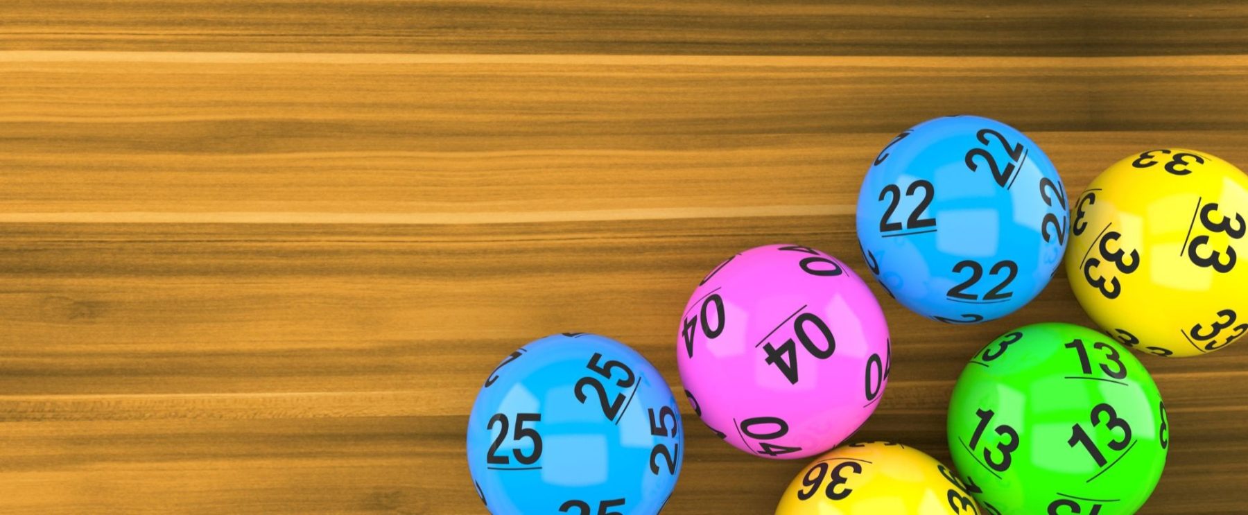 Five lottery balls rest on a wooden table: a blue ball numbered 25, a pink ball numbered 04, another blue ball numbered 22, a yellow ball numbered 33, and a green ball numbered 13