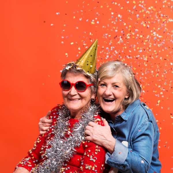 Celebration photo, 2 women joyfully smiling, wearing hats and surrounded by confetti