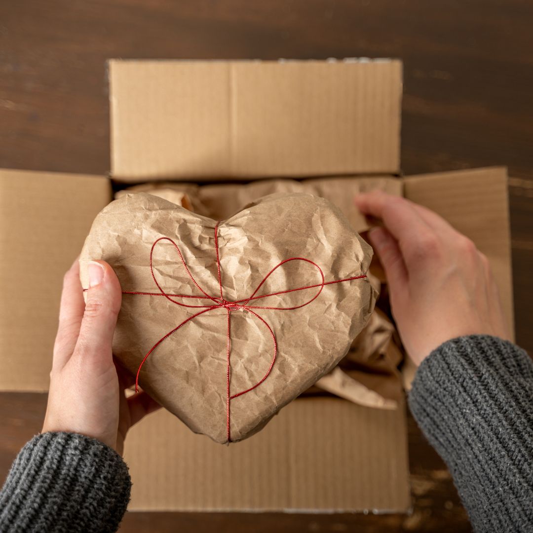 gift aid - person holding a heart-shaped gift above a cardboard box